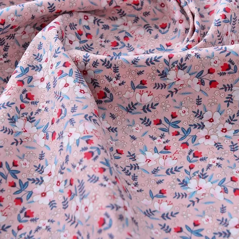 Gros plan sur le tissu popeline de coton imprimé au mètre 100% coton de Longan Craft France, qui présente un motif floral avec des fleurs blanches, rouges et bleues et des feuilles vertes - idéal pour le bricolage, le quilting, les peignoirs, les chemises et les langes.