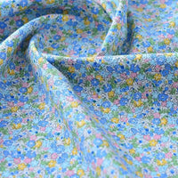 Gros plan sur le tissu popeline de coton imprimé au mètre de Longan Craft France, 100 % coton avec un imprimé floral bleu clair, doucement drapé pour montrer sa texture lisse - idéal pour le bricolage, le quilting, les nappes, les robes et les chemises.