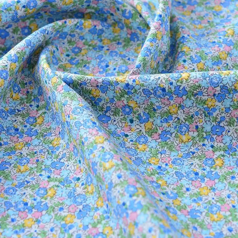 Gros plan sur le tissu popeline de coton imprimé au mètre de Longan Craft France, 100 % coton avec un imprimé floral bleu clair, doucement drapé pour montrer sa texture lisse - idéal pour le bricolage, le quilting, les nappes, les robes et les chemises.