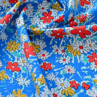 Un gros plan du tissu popeline de coton imprimé au mètre de Longan Craft France, 100% coton, à motifs floraux colorés sur fond bleu, idéal pour DIY, quilting, nappes, robes et chemises. Popeline unie 40S souple et légèrement plissée.