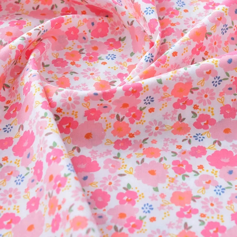 Un gros plan du tissu popeline de coton imprimé au mètre de Longan Craft France, unie 40S 100 % coton, montre un motif floral coloré avec des fleurs roses, orange et violettes sur fond blanc. Idéal pour DIY, quilting, nappes, robes et chemises.
