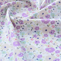 Gros plan sur le Tissu popeline de coton imprimé au mètre de Longan Craft France, 100% coton à motifs floraux, montrant des fleurs violettes, roses et bleues sur fond clair. Parfait pour DIY, quilting, nappes, robes et chemises.
