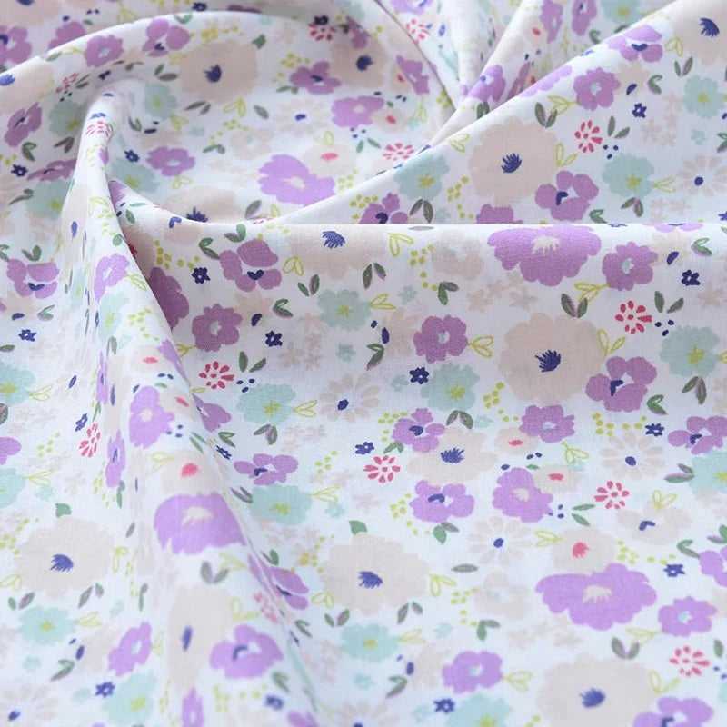 Gros plan sur le Tissu popeline de coton imprimé au mètre de Longan Craft France, 100% coton à motifs floraux, montrant des fleurs violettes, roses et bleues sur fond clair. Parfait pour DIY, quilting, nappes, robes et chemises.