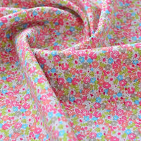 Gros plan sur le Tissu popeline de coton imprimé au mètre de Longan Craft France, un tissu 100% coton avec de petits motifs floraux roses, orange, bleus et gris sur un fond clair - idéal pour le bricolage, le quilting, les nappes, les robes et les chemises.
