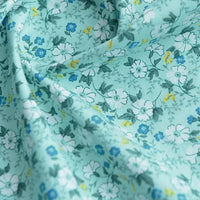 Tissu popeline de coton imprimé au mètre 100% coton "Longan Craft France" avec motifs floraux, idéal pour DIY, quilting, nappes, robes et chemises. Popeline légère bleue claire à petites fleurs blanches, bleues et jaunes avec feuilles vertes.