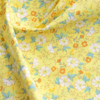 Un gros plan du Tissu popeline de coton imprimé au mètre par Longan Craft France montre ses motifs floraux 100% coton avec des fleurs blanches, orange et des feuilles vertes. La popeline unie 40S se caractérise par des plis souples et une texture lisse de haute qualité.