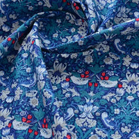 Un gros plan du tissu popeline de coton imprimé au mètre (Popeline unie 40S, 100 % coton) de Longan Craft France montre son motif floral complexe avec des fleurs blanches et bleues, des feuilles vertes et des baies rouges. Le tissu est légèrement froissé et drapé.