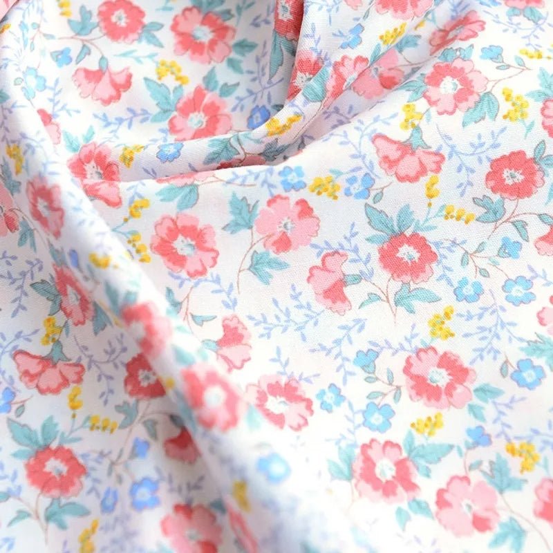 Un gros plan de Longan Craft France Tissu popeline de coton imprimé au mètre, 100% coton avec motifs floraux colorés sur fond blanc, idéal pour DIY, quilting, nappes, robes et chemises. Le tissu drape doucement avec de légères ondulations.