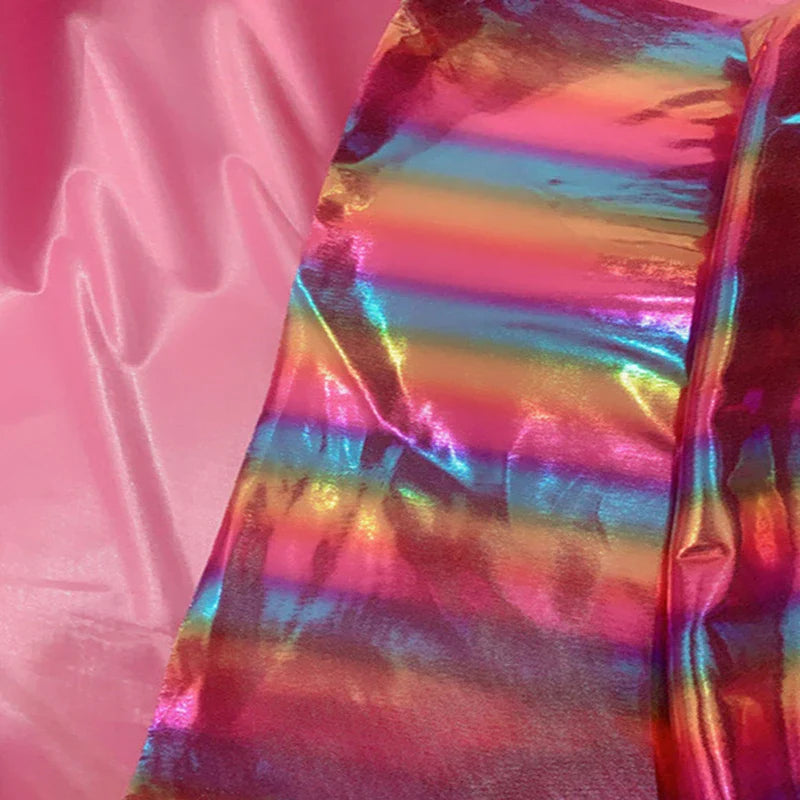Une bande de Tissu lamé arc-en-ciel au mètre de Longan Craft France, polyester irisé à rayures dégradées, reflète des teintes métalliques vives à côté d'un tissu rose mat-parfait pour costumes de scène ou événements spéciaux.