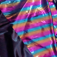Le tissu lamé arc-en-ciel au mètre de Longan Craft France, en polyester irisé à rayures dégradées roses, orange et bleues avec partie noire, offre une finition métallique idéale pour costumes de scène ou événements spéciaux.