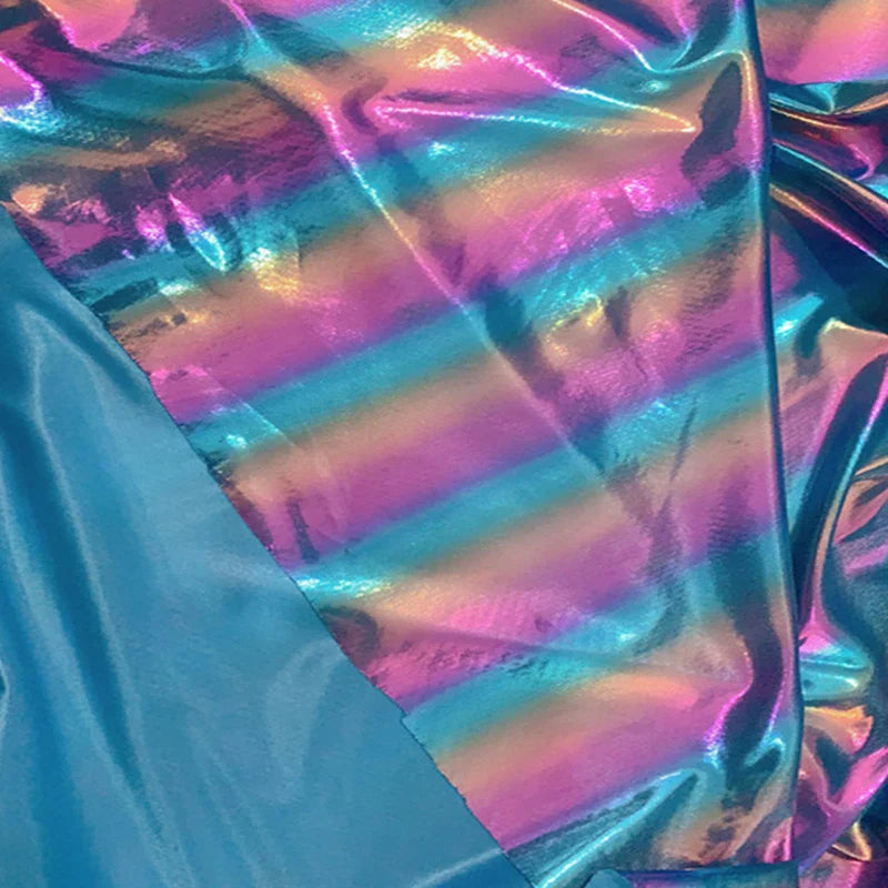Un tissu lamé arc-en-ciel au mètre de Longan Craft France, en polyester irisé à rayures dégradées bleu, rose et violet, brille à côté d'un tissu bleu mat-parfait pour costumes de scène ou tenues d'événements spéciaux.