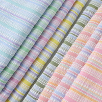 Plusieurs pièces de Tissu seersucker rayé arc-en-ciel de Longan Craft France, en polyester léger, sont disposées côte à côte. Elles présentent des rayures pastel bleues, vertes, jaunes, roses et violettes sur un fond clair.