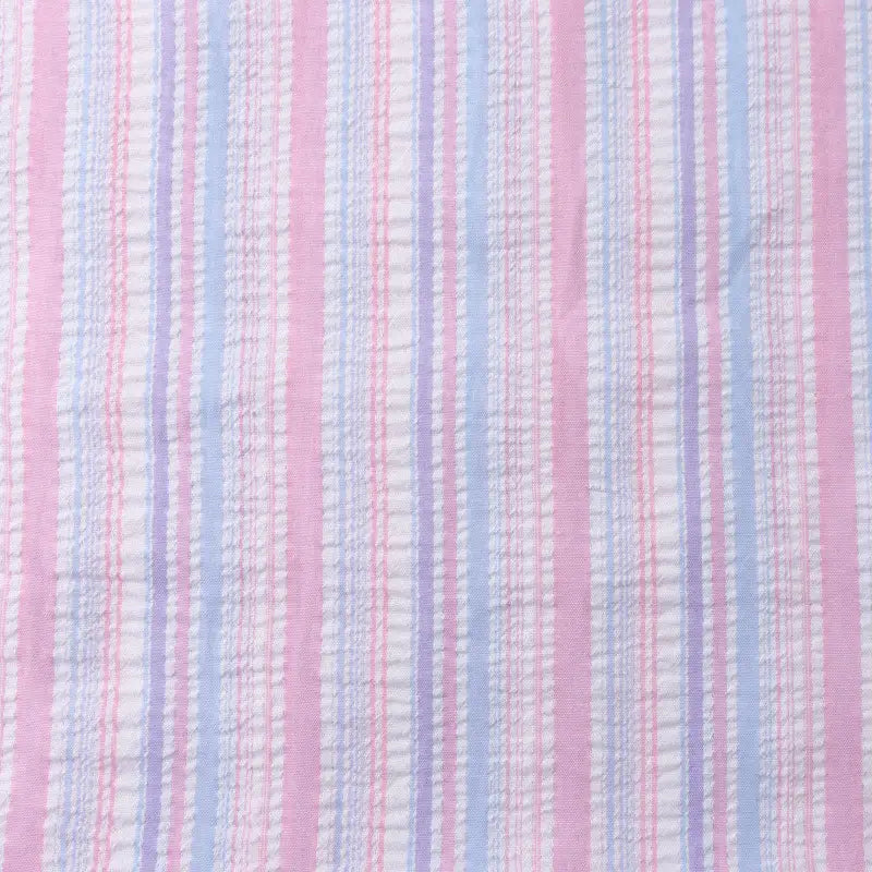 Un gros plan du tissu seersucker rayé arc-en-ciel au mètre de Longan Craft France montre un tissu polyester rayé coloré avec une surface texturée et légèrement froissée, idéal pour les robes et autres projets créatifs.