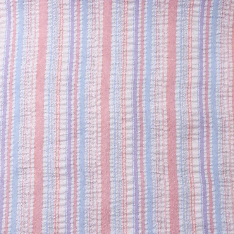 Un gros plan du tissu seersucker rayé arc-en-ciel au mètre de Longan Craft France montre ses rayures verticales colorées en rose, bleu, blanc, avec de fines lignes rouges et une texture polyester légèrement froissée, idéale pour les robes.