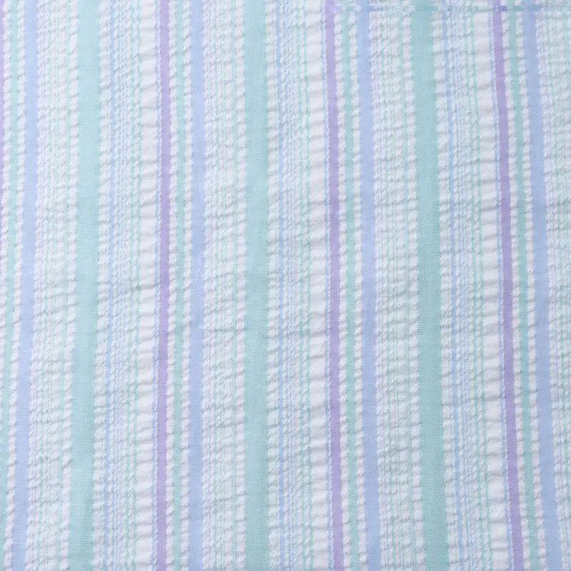 Un gros plan du tissu seersucker rayé arc-en-ciel au mètre de Longan Craft France montre des rayures verticales colorées dans des tons pastel sur fond blanc. Ce tissu en polyester est légèrement texturé, idéal pour les robes et les projets de couture créatifs.