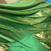 Gros plan sur le tissu satin lamé au mètre de Longan Craft France, un tissu en polyester métallisé et brillant, dont les plis et les couches vertes brillantes sont idéales pour la couture, les robes de chambre et les travaux manuels, alors que la lumière révèle des nuances variées.