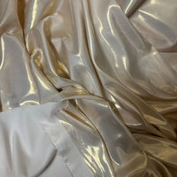 Gros plan sur le tissu satin lamé au mètre de Longan Craft France, un lamé de polyester beige clair brillant idéal pour les robes DIY et les travaux manuels, avec des bords de tissu blanc non finis visibles dans le coin.