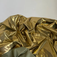 Un morceau de tissu Longan Craft France satin lamé au mètre, polyester métallisé et brillant, est étalé avec une section de tissu vert olive mat devant sur un fond clair uni, parfait pour les robes de bricolage et les travaux manuels.