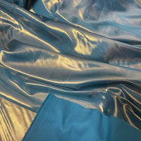 Le satin bleu clair brillant lamé au mètre de Longan Craft France se déploie en plis souples, avec un soupçon de tissu de robe bleu mat au premier plan.
