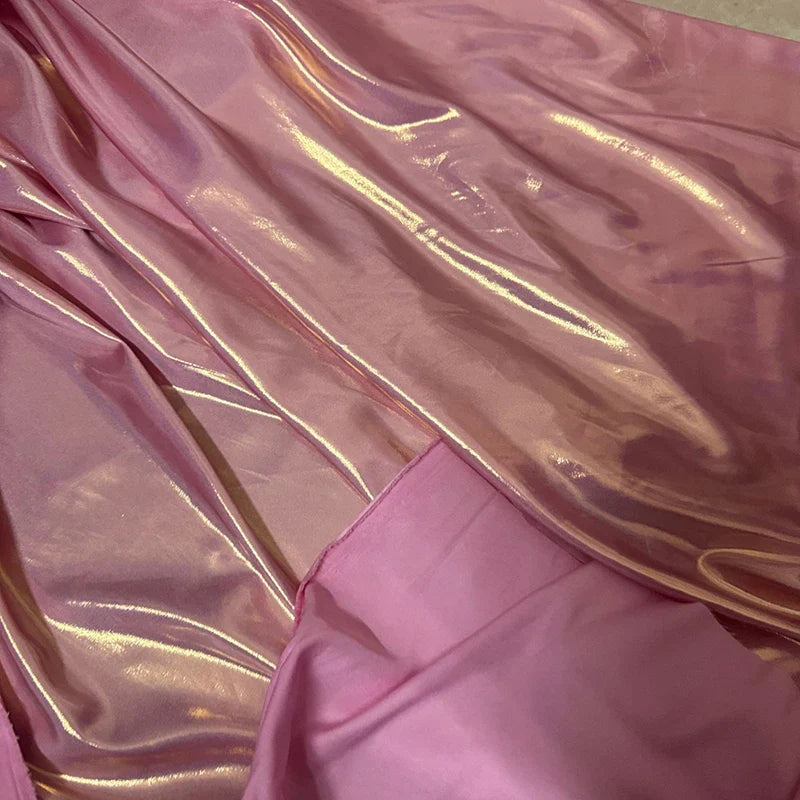 Un gros plan du Tissu satin lamé au mètre de Longan Craft France montre sa surface brillante en polyester métallisé superposée à un rose mat, reflétant la lumière-idéal pour couture, robes DIY ou travaux manuels.