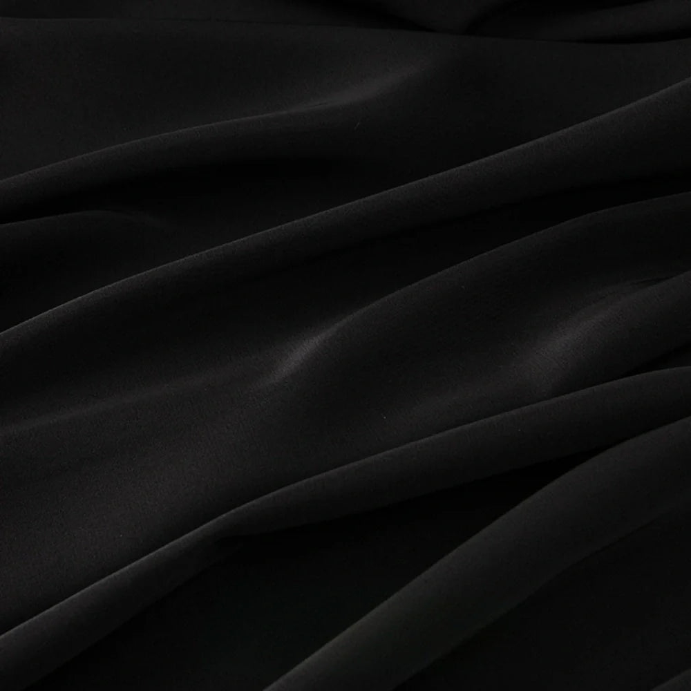 Gros plan sur le tissu mousseline satiné au mètre de Longan Craft France en noir, qui présente des plis souples et fluides - idéal pour les robes de soirée élégantes. Ce tissu extensible et soyeux est parfait pour créer des vêtements luxueux.