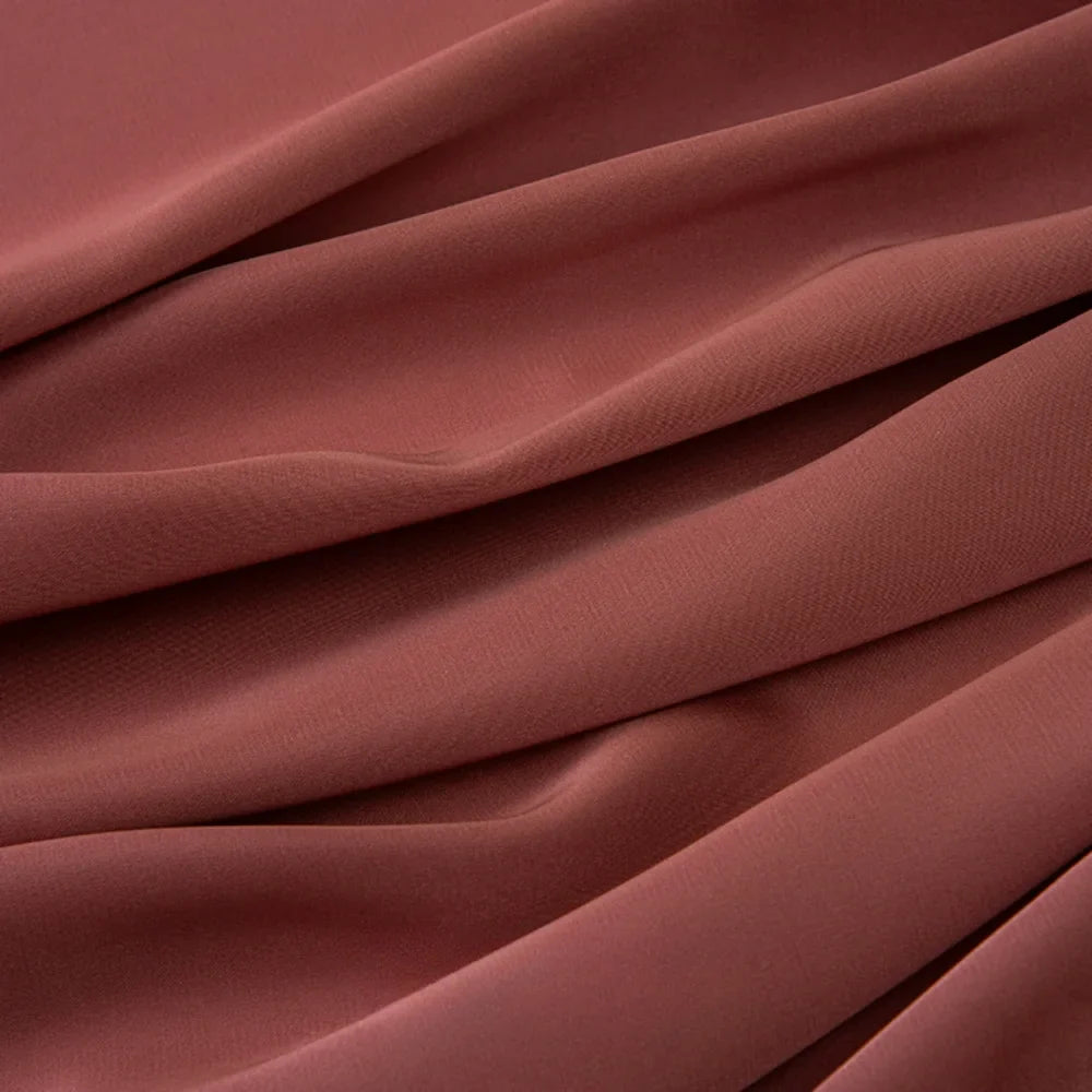 Le tissu mousseline satinée au mètre de Longan Craft France montre en gros plan ses plis lisses de couleur brun rosé. Ce tissu extensible et doux est idéal pour les robes et les vêtements de soirée élégants. Mousseline soyeuse par excellence.