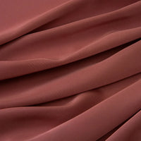 Le tissu mousseline satinée au mètre de Longan Craft France montre en gros plan ses plis lisses de couleur brun rosé. Ce tissu extensible et doux est idéal pour les robes et les vêtements de soirée élégants. Mousseline soyeuse par excellence.
