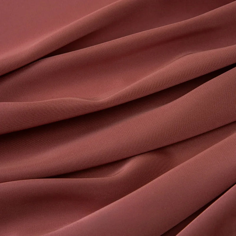 Le tissu mousseline satinée au mètre de Longan Craft France montre en gros plan ses plis lisses de couleur brun rosé. Ce tissu extensible et doux est idéal pour les robes et les vêtements de soirée élégants. Mousseline soyeuse par excellence.