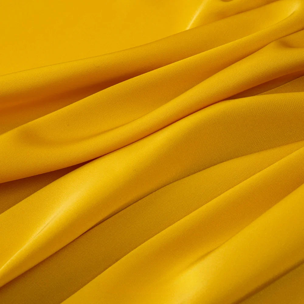 Gros plan sur le Tissu mousseline satinée au mètre de Longan Craft France, qui présente des plis lisses, jaune vif et brillants, semblables à du satin. Cette mousseline extensible et douce est idéale pour les vêtements et est disponible au mètre.