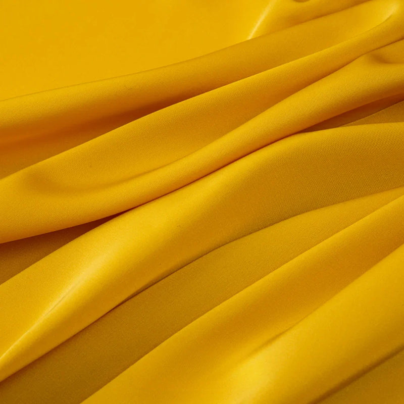 Gros plan sur le Tissu mousseline satinée au mètre de Longan Craft France, qui présente des plis lisses, jaune vif et brillants, semblables à du satin. Cette mousseline extensible et douce est idéale pour les vêtements et est disponible au mètre.