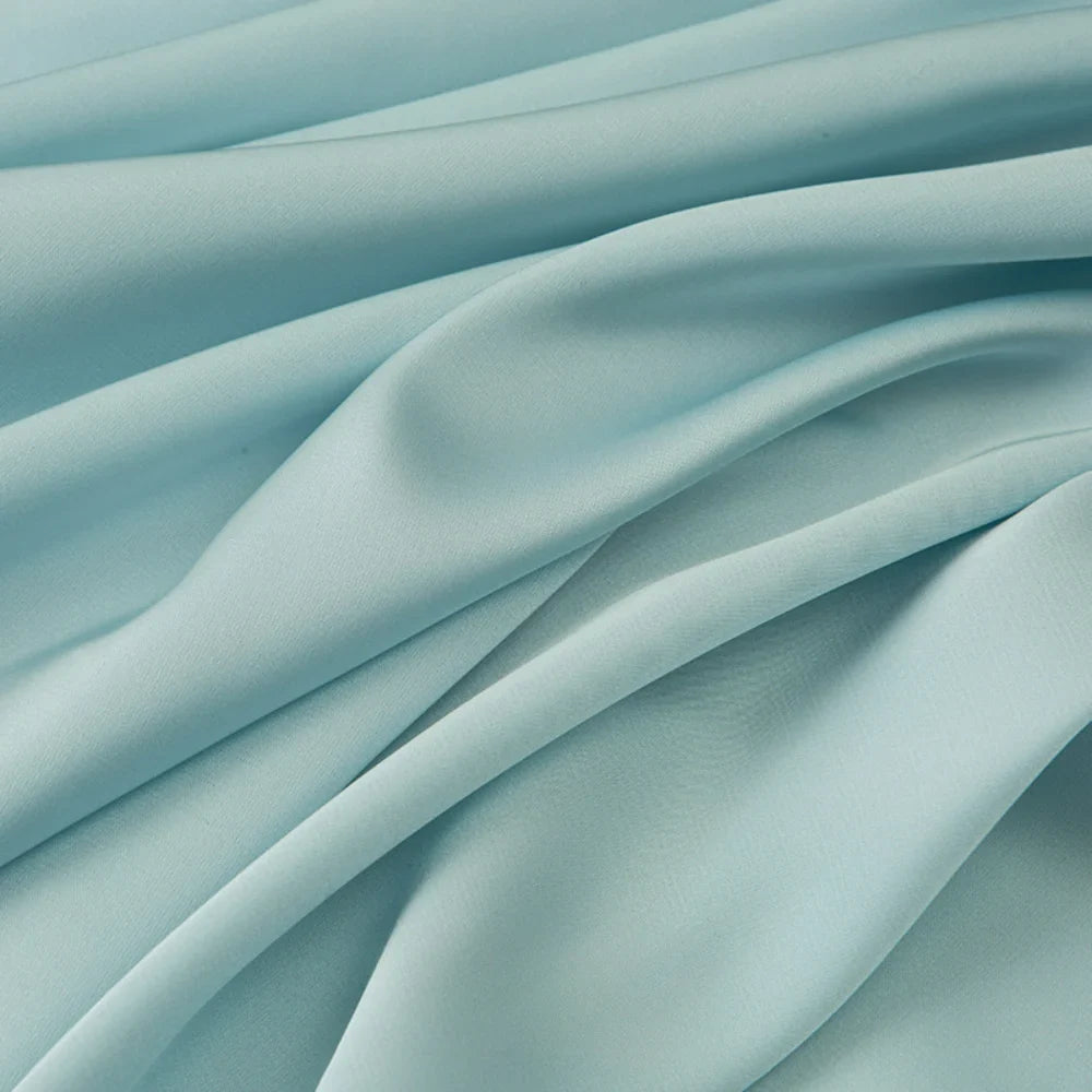 Tissu mousseline satinée au mètre de Longan Craft France, extensible et doux, apparaît en gros plan avec de délicats plis et une texture lisse. Parfait pour une robe soirée élégante ou d'autres vêtements grâce à sa brillance soyeuse.