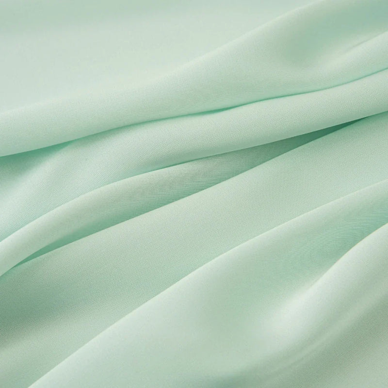 Découvrez le Tissu mousseline satinée au mètre de Longan Craft France - vert clair, extensible, soyeux et subtilement brillant. Parfait pour les robes de soirée élégantes ou les créations personnalisées avec son drapé doux et ses plis délicats.