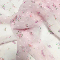 Un gros plan du tissu mousseline à petites fleurs au mètre de Longan Craft France montre son délicat imprimé floral rose, violet et vert sur un tissu diaphane aéré, parfait pour les robes d'été élégantes et les projets créatifs.