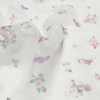 Le tissu mousseline à petites fleurs au mètre de Longan Craft France : des plumetis blancs transparents à la texture subtilement pointillée, imprimés de petites roses roses et violettes et de feuilles vertes - parfaits pour les robes d'été.