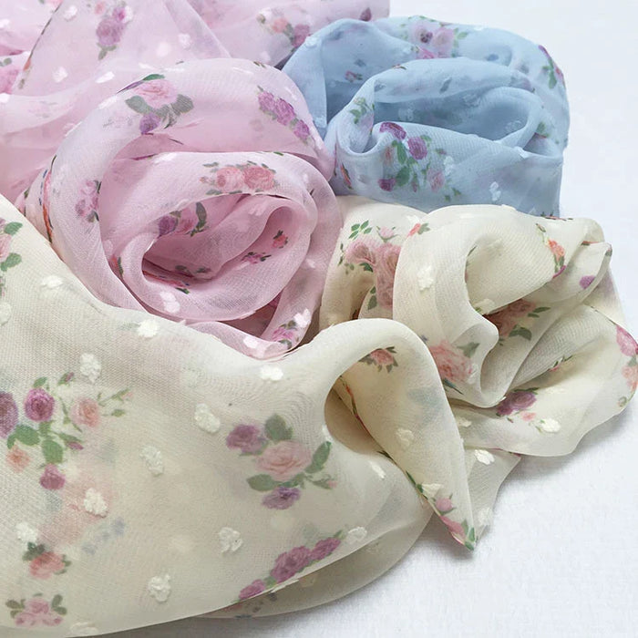 Trois pièces de tissu mousseline imprimé fleurs plumetis de Longan Craft France, présentées dans des tons pastels rose pâle, bleu pâle et crème, sont délicatement rassemblées sur une surface légère. Tissu créateur idéal pour les robes d'été, vendu au mètre.