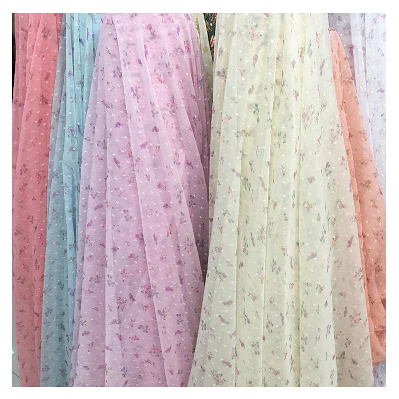 Plusieurs rouleaux de tissu mousseline à petites fleurs de Longan Craft France dans des tons pastel - rose, bleu, lavande, blanc, pêche - se tiennent debout. Chacun d'entre eux présente de délicats imprimés floraux en plumetis, parfaits pour les robes d'été.