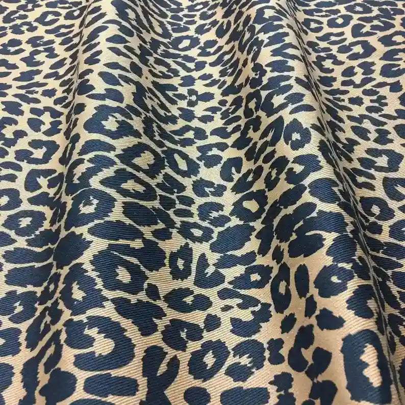 Gros plan sur le Tissu jean imprimé léopard 10oz de Longan Craft France, un denim 100% coton délavé noir et beige, drapé pour révéler son audacieux motif léopard et sa riche texture sergée.