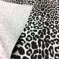 Gros plan sur le Tissu jean imprimé léopard 10oz de Longan Craft France, un denim 100 % coton délavé avec un imprimé léopard noir et blanc, dont un coin est retourné pour révéler le motif inversé, plus clair et moins distinct.