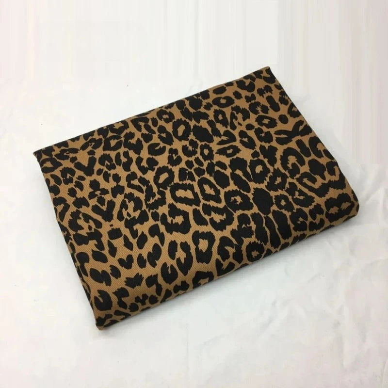 Un morceau plié de Tissu jean imprimé léopard 10oz de Longan Craft France, présentant un motif léopard marron et noir dans un denim 100 % coton lavé, est présenté sur une surface blanche.