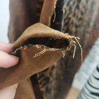 Le Tissu jean imprimé léopard 10oz au mètre-un tissu denim lavé 100% coton au motif léopard remarquable de Longan Craft France est encadré par un gros plan d'une main tenant un tissu marron effiloché dont les fils se détachent.