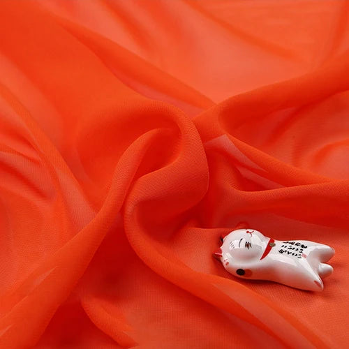 Mousseline légère transparente au mètre" de Longan Craft France, orange vif, drapée de plis souples, à côté d'une petite figurine de chat en céramique blanche avec des détails rouges et noirs.