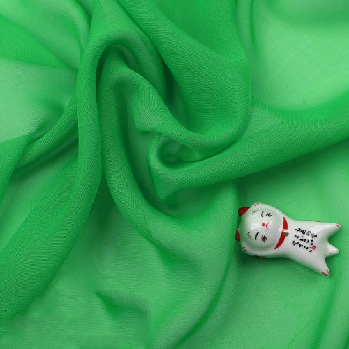 Un petit chat blanc en céramique avec des accents rouges repose sur une Mousseline légère transparente de Longan Craft France, un tissu en polyester fin et doux vendu au mètre.