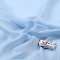 Une petite figurine de chat en céramique avec des détails peints est présentée sur la mousseline légère transparente au mètre de Longan Craft France, une mousseline douce et fine en tissu de polyester disponible au mètre.