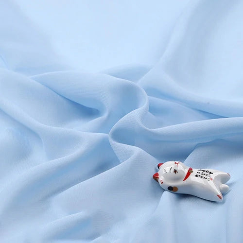 Une petite figurine de chat en céramique avec des détails peints est présentée sur la mousseline légère transparente au mètre de Longan Craft France, une mousseline douce et fine en tissu de polyester disponible au mètre.