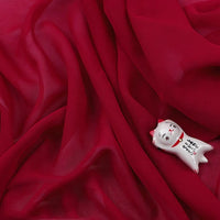 Une petite figurine de chat blanc avec des marques rouges et une écriture noire repose sur de la Mousseline légère transparente au mètre de Longan Craft France, créant un effet délicat et semi-transparent.