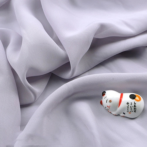 Une figurine de chat en céramique blanche aux détails peints repose sur la mousseline légère transparente de Longan Craft France, une mousseline en tissu de polyester doux et fin vendue au mètre.