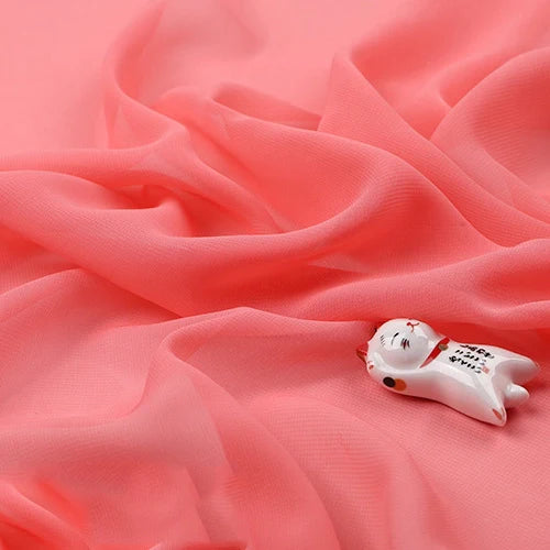 Une petite figurine de chat en céramique repose sur une Mousseline légère transparente au mètre de Longan Craft France, une fine mousseline en tissu de polyester qui s'étale uniformément et remplit la plus grande partie de l'image.