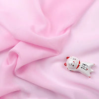 Une petite figurine de chat blanc en céramique avec des accents rouges repose sur la mousseline légère transparente au mètre de Longan Craft France, une mousseline douce et fine en tissu de polyester qui évoque le charme délicat des tenues de soirée.
