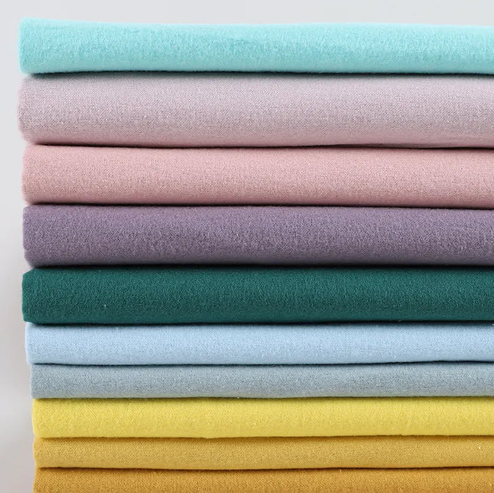 Une pile bien rangée de Flanelle de coton uni au mètre de Longon Craft France dans des couleurs unies assorties - bleu, rose, violet, vert, jaune, sarcelle - offre un tissu flanellette super doux pour des quilts d'automne douillets et des projets câlins.
