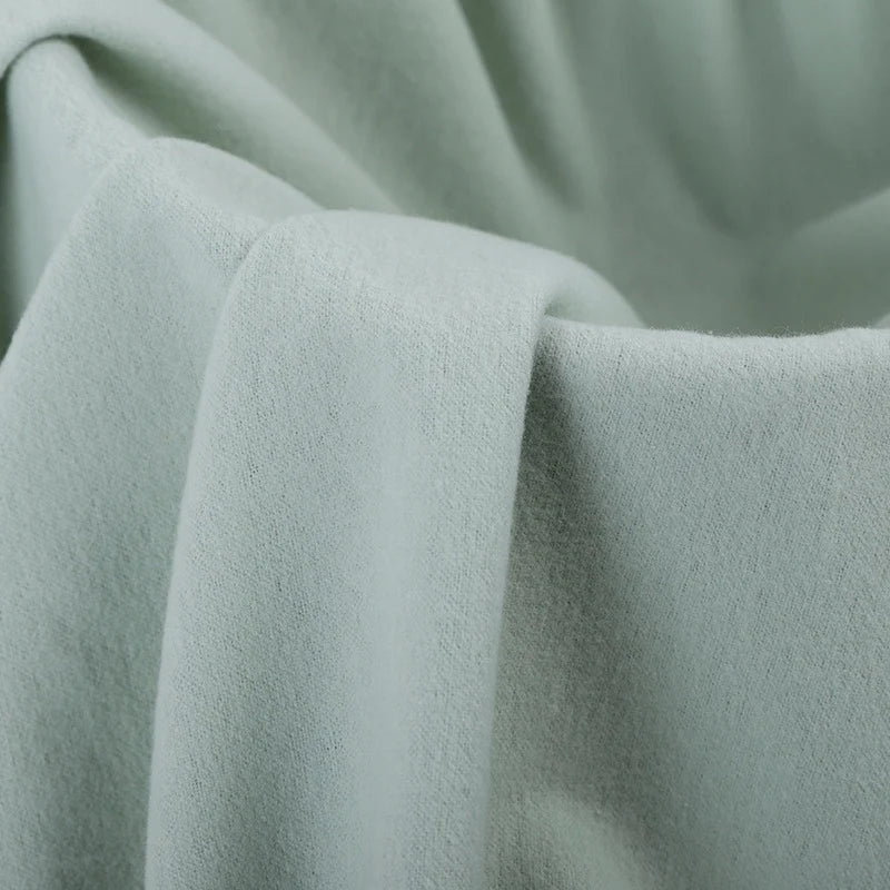 Un gros plan de la Flanelle de coton uni au mètre de Longon Craft France montre sa couleur vert clair, sa texture super douce et ses plis délicats - une flanellette ultra-confortable parfaite pour pyjamas et câlins d'automne.